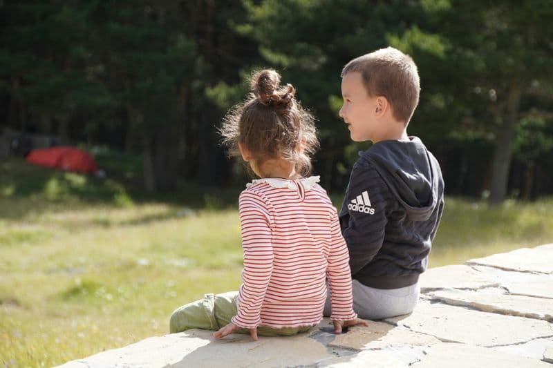 a couple of children sitting on a concrete ledge looking at each other