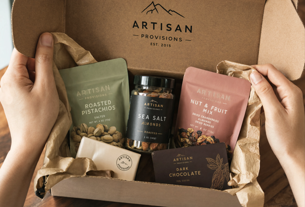 Hands opening a branded gourmet gift box containing nuts, almonds and dark chocolate on a wooden surface