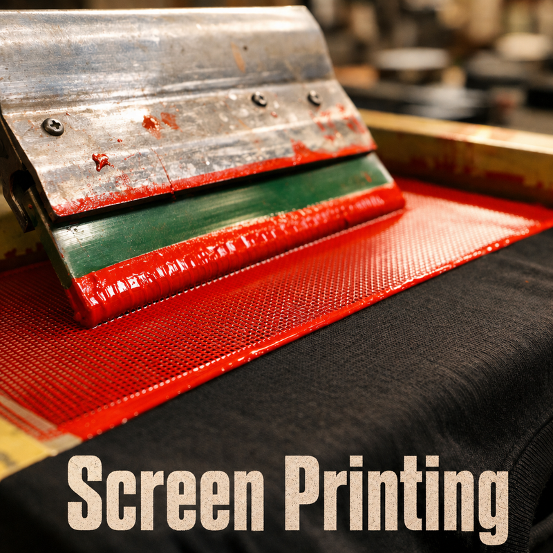 A squeegee pressing red and white ink through a screen onto black fabric during the screen printing process