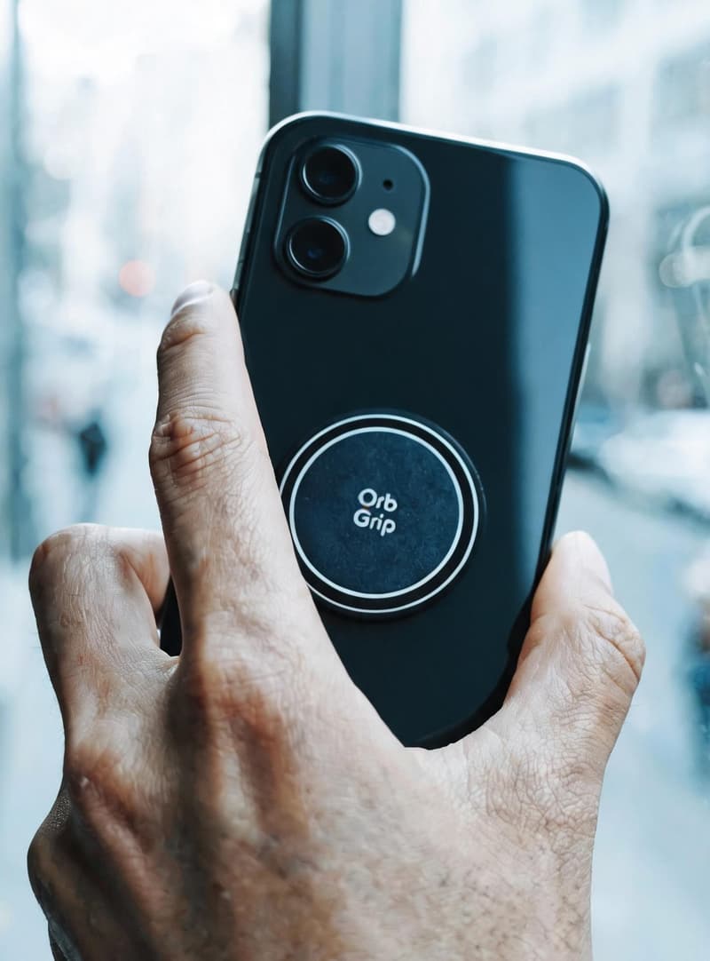 Hand holding a smartphone with a branded circular grip attached to the back