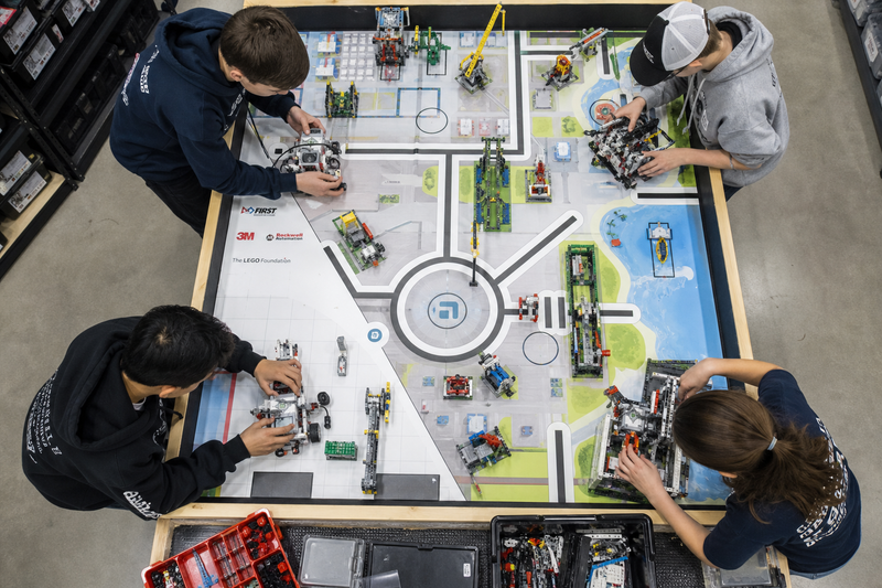 Students collaborating on a FIRST LEGO League style LEGO robot and laptop, showing robotics programming, teamwork, and hands-on competition preparation.