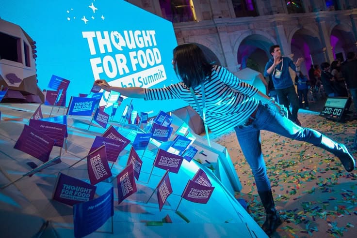 This may contain: a woman standing on top of a table next to a giant screen with purple and blue signs