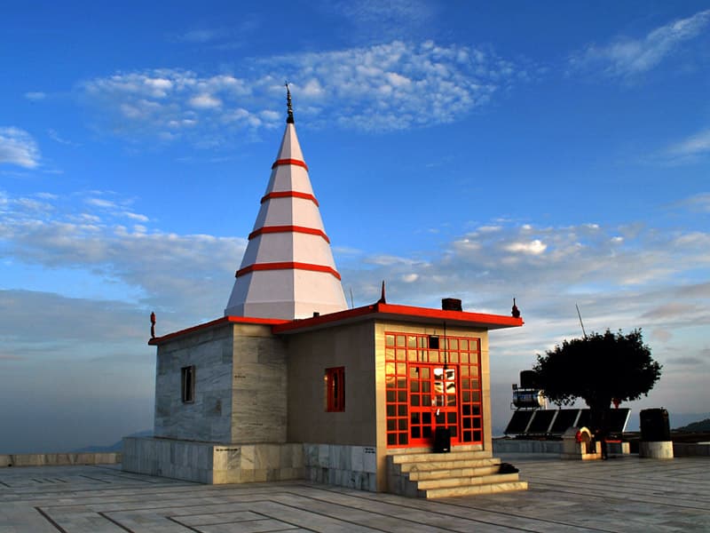 स्वच्छ नीले आकाश और श्वेत मेघों के नीचे स्थित काली का टिब्बा मंदिर का विस्तृत कोण से लिया गया छायाचित्र।