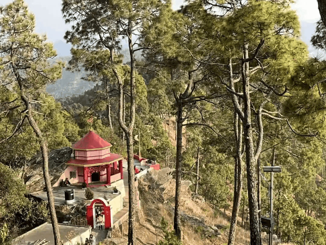A photo of Kasardevi Temple, Almora (Uttarakhand), captured from a top-view. A statue of Nandi faces the main temple’s entrance door. It is painted red and situated on a hill right next to a valley.