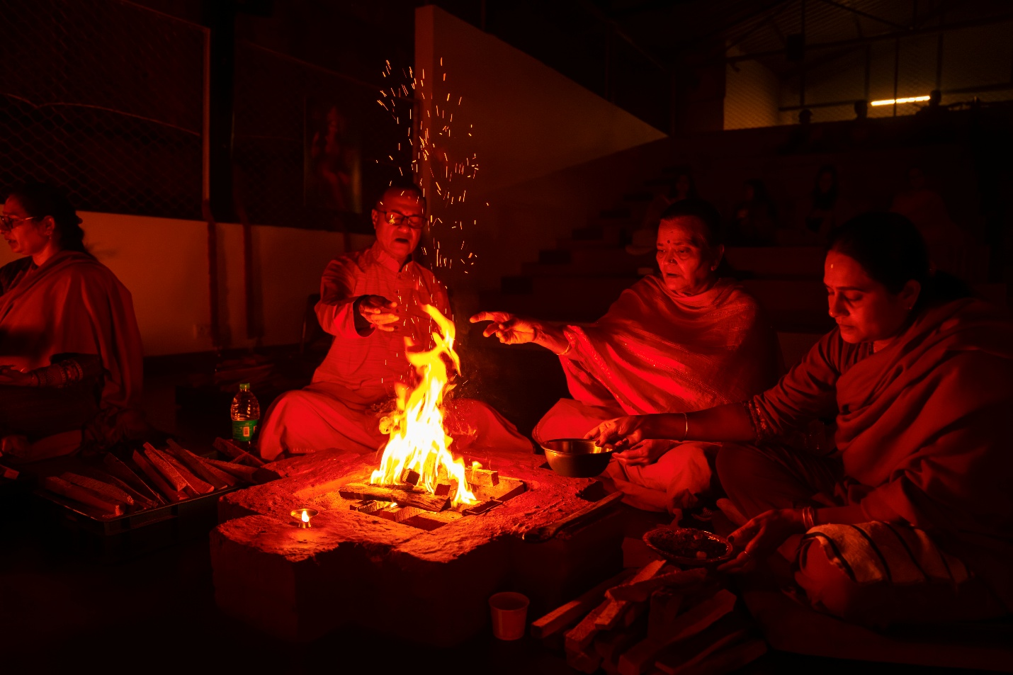 A dimly lit photo of 3 Hindu devotees making offerings to the sacred fire in a Yagna.