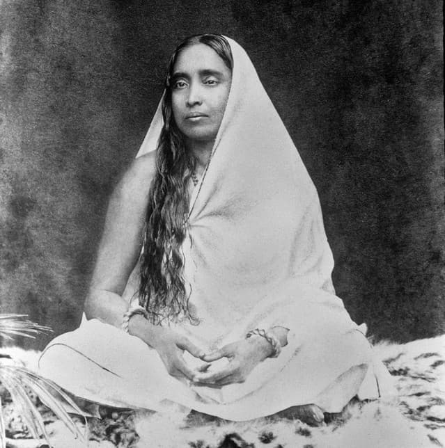 A real black-and-white photo of Sri Sarada Devi, Swami Ramakrishna Paramahamsa's wife, sitting cross-legged.
