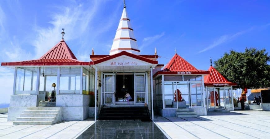 स्वच्छ नीले आकाश और श्वेत मेघों के नीचे स्थित काली का टिब्बा मन्दिर का सम्मुख-दृश्य छायाचित्र।