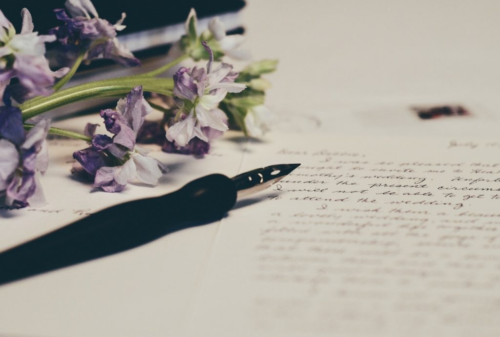 A black pen sits on top of a personalised letter next to some purple flowers