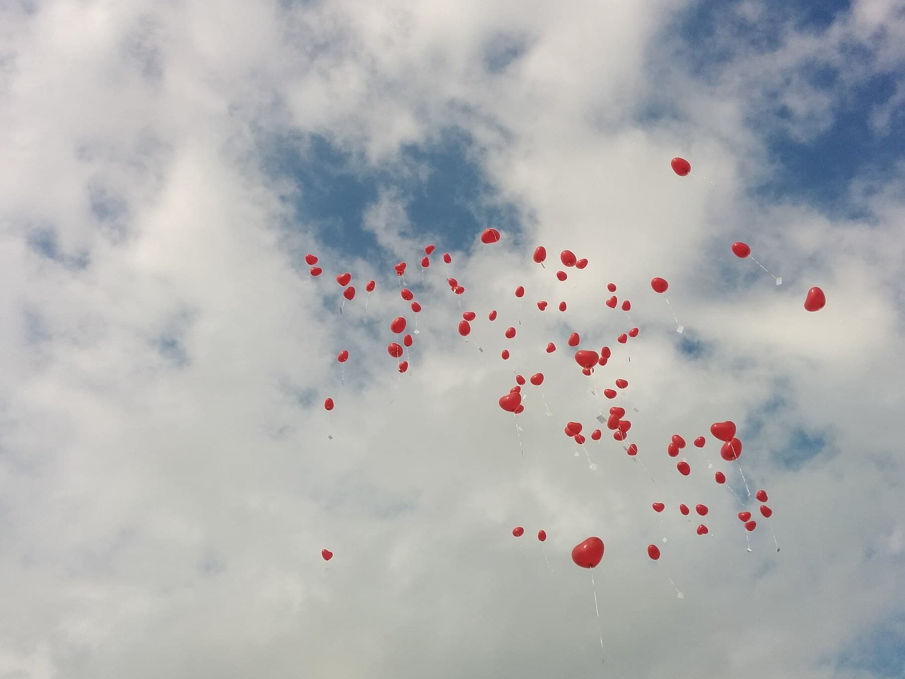 Red heart balloons floating in a blue sky
