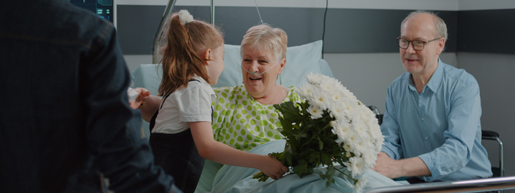 Old patient receiving visit from child and mother in hospital ward with flowers