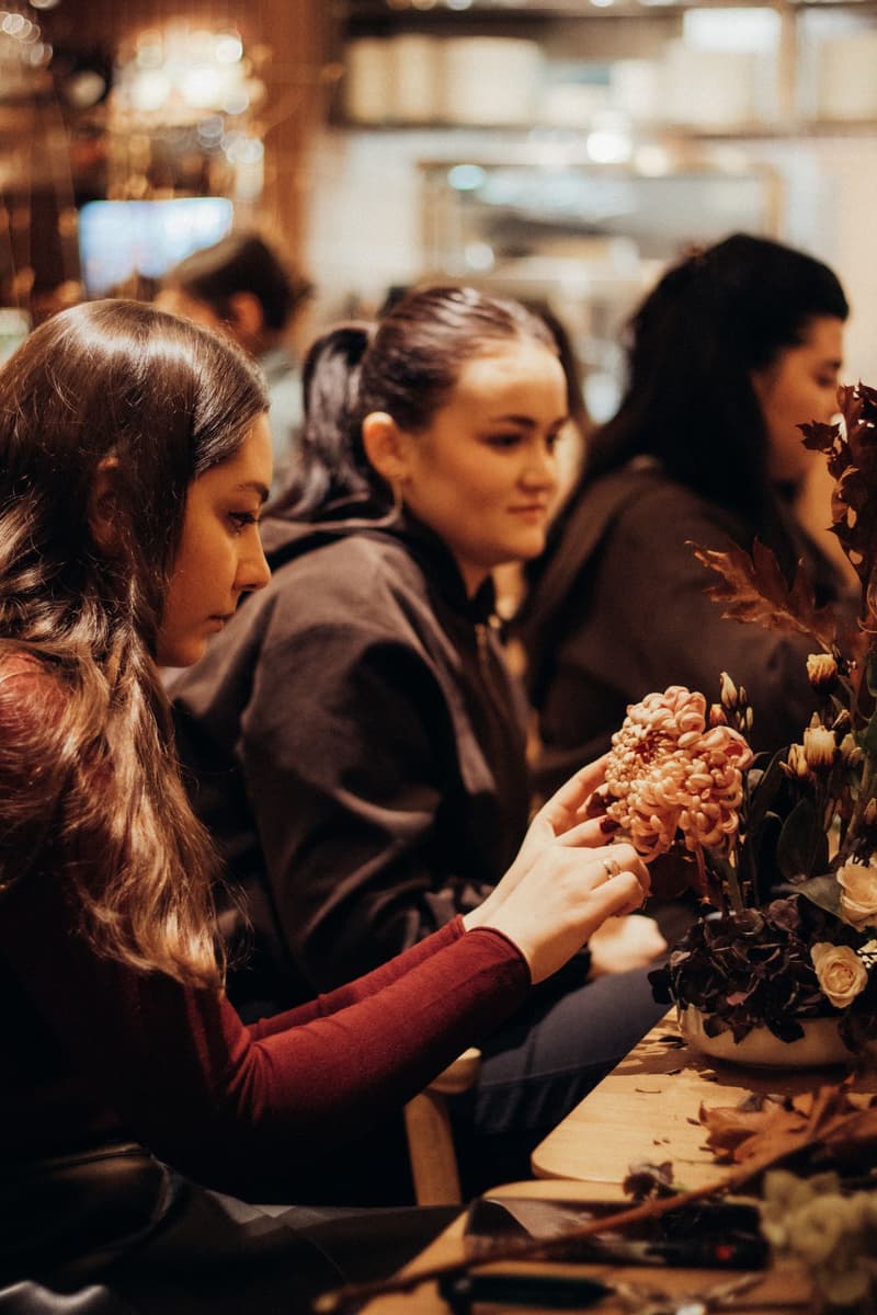 Women at a floristry workshop arranging chrysanthemums, roses and autumn leaves in a low bowl