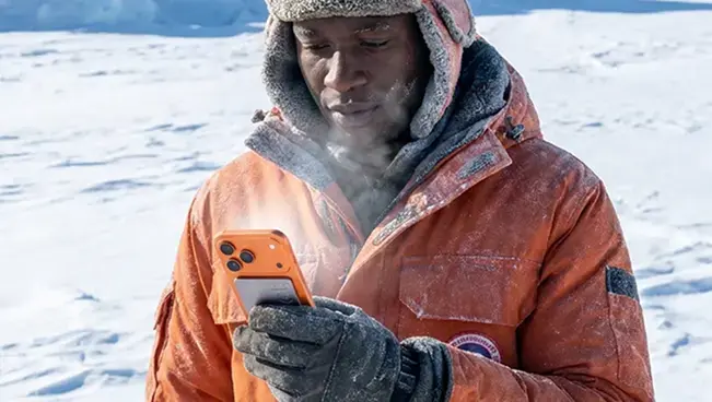 A man in an orange parka using a Pocket-equipped phone in heavy snow